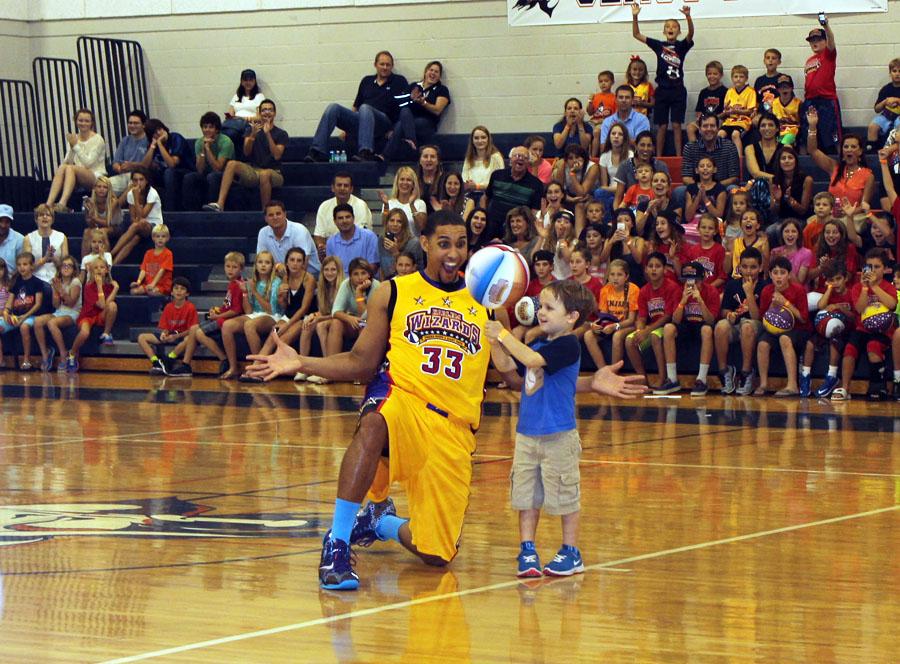 Harlem Wizard DP looks on in amazement as a young fan at the game spins a basketball on a pen. Crowd-pleasing antics such as this one is what made the game so entertaining.