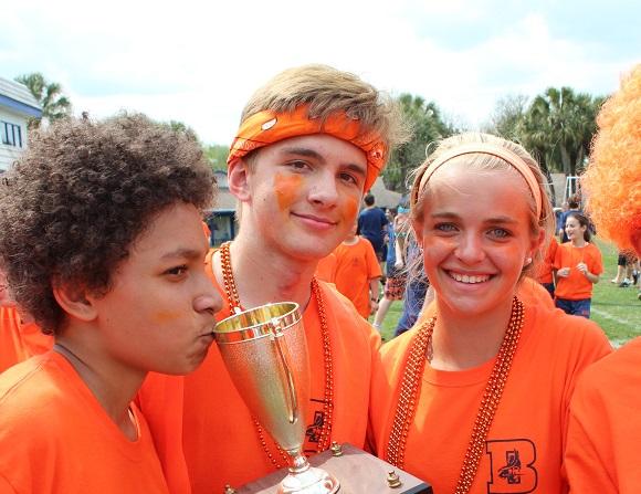 Eighth-grader Garison Gelman kisses the Field Day trophy alongside Orange co-captains John Scott and Tati Ziff.