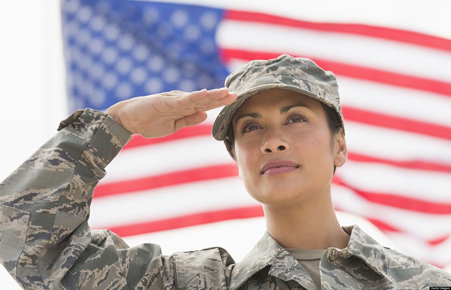 A female soldier salutes with the American flag in the background.