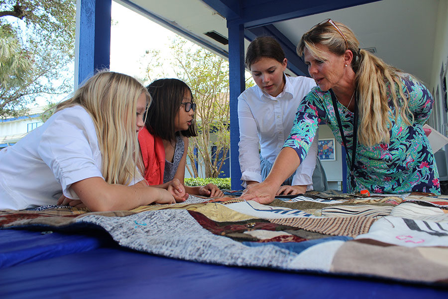 During Heritage Day, sixth graders Winni Cox, Claire Dinh, and Ellie Bickel join lower school science teacher Mrs. Susan Bickel in admiring the craftsmanship of one of the quilts the students sewed. 
