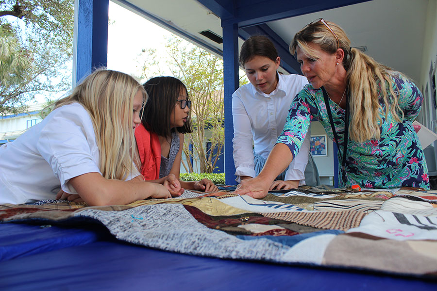 During Heritage Day, sixth graders Winni Cox, Claire Dinh, and Ellie Bickel join lower school science teacher Mrs. Susan Bickel in admiring the craftsmanship of one of the quilts the students sewed.