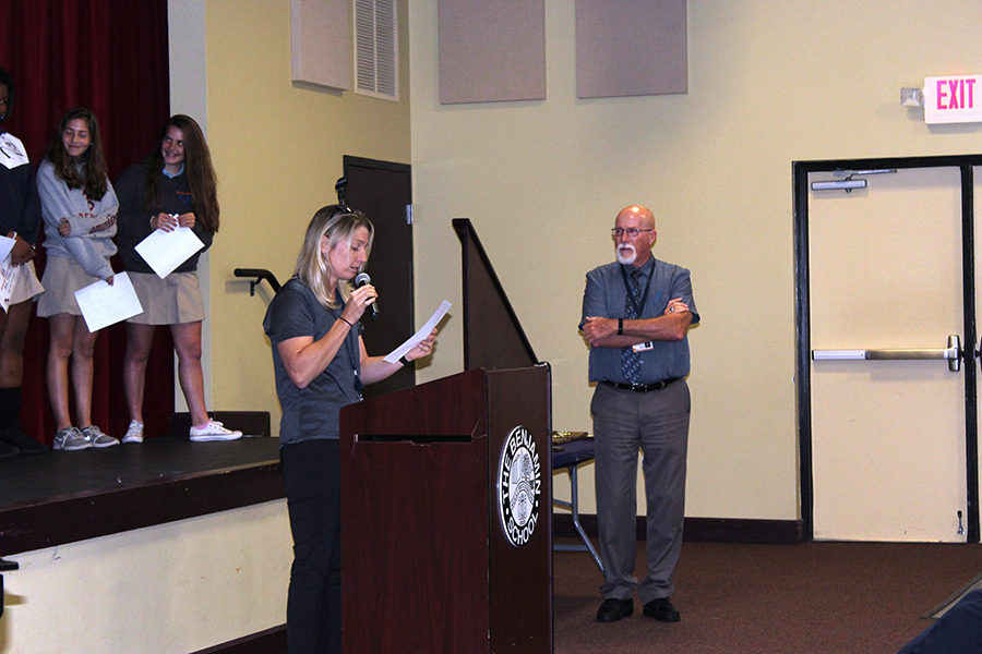 With the team standing on stage behind her, Ms. Filia talks about the girls basketball season as Mr. Mullnix looks on.