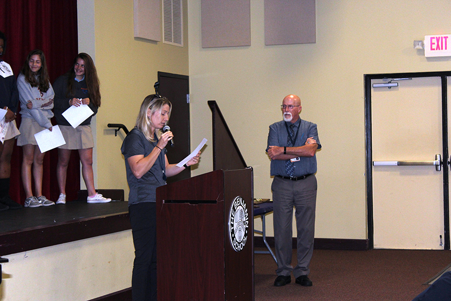 With the team standing on stage behind her, Ms. Filia talks about the girls' basketball season as Mr. Mullnix looks on.